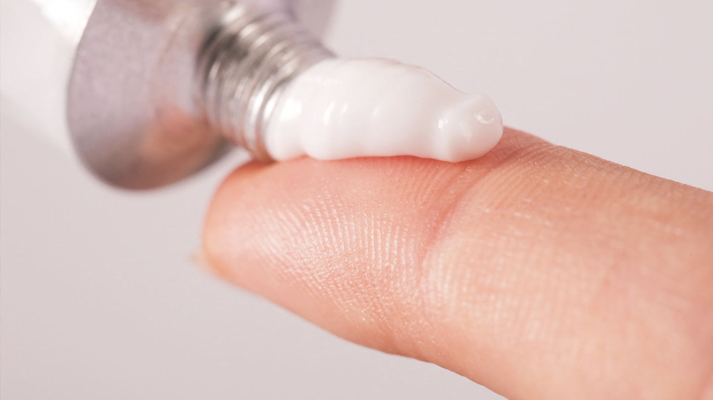 Kortisonsalbe richtig anwenden Kortisonsalbe: Ein kurzer weißer Salbenstrang wird aus einer Tube auf die Fingerspitze gedrückt.