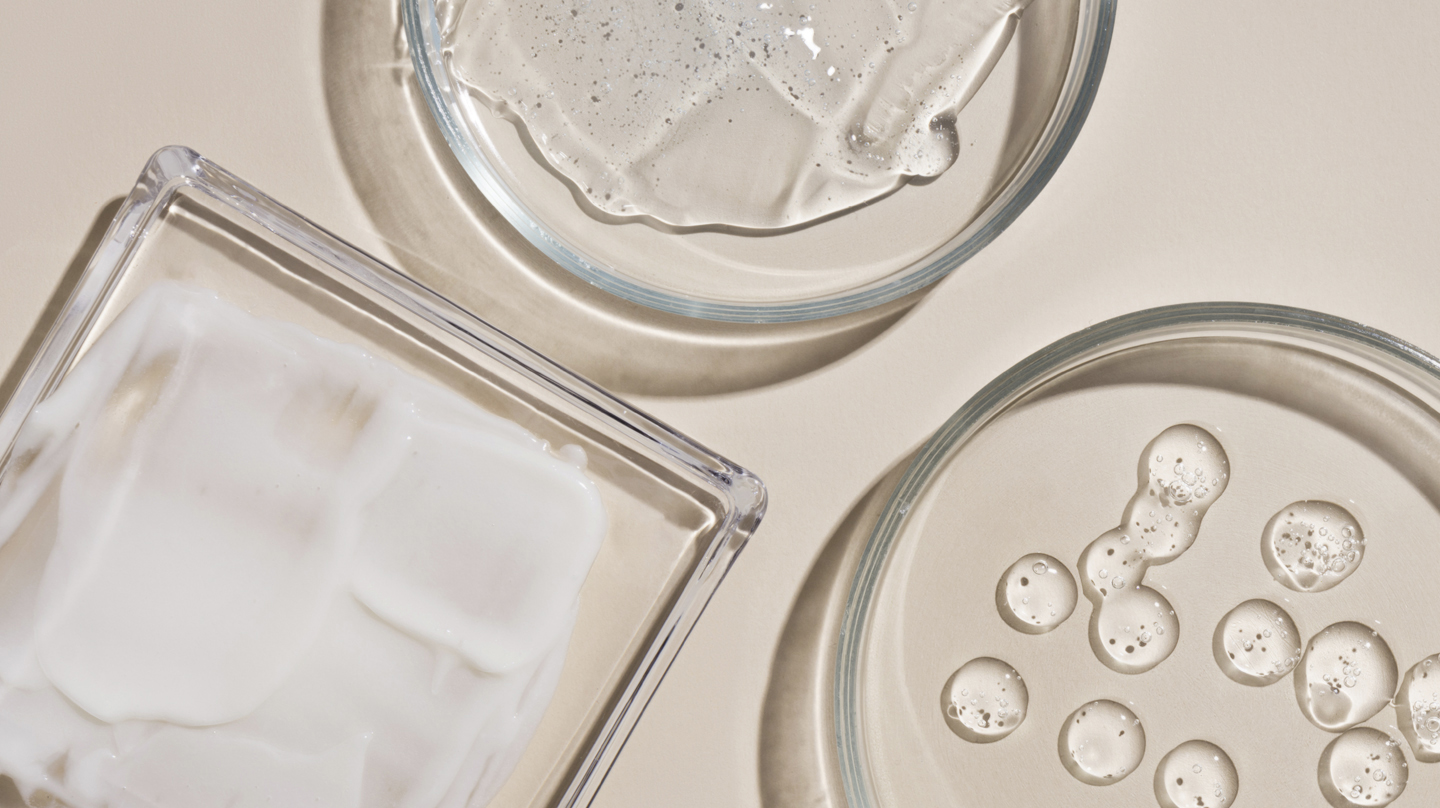 Retinol – mehr Frische für die Haut Retinol: Drei flache Glasschalen auf beiggrauem Grund, darin ein transparentes Gel ausgestrichen bzw. in Form von Tropfen.