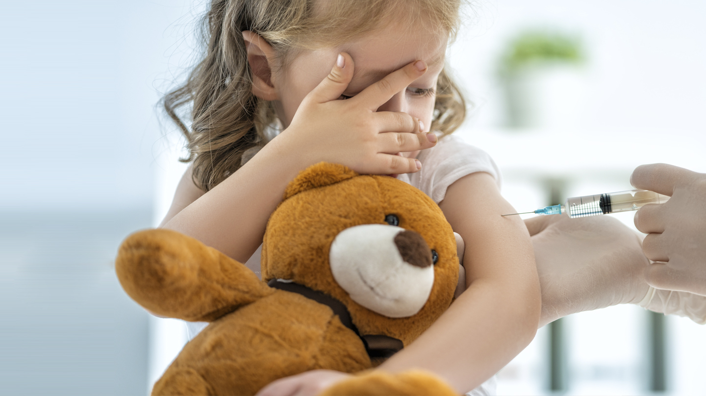 Menschenskinder – keine Angst vor Spritzen Angst vor Spritzen: Kleines Mädchen mit Teddybär im Arm schaut skeptisch auf die Spritze, die ihr der Arzt gerade verabreicht.